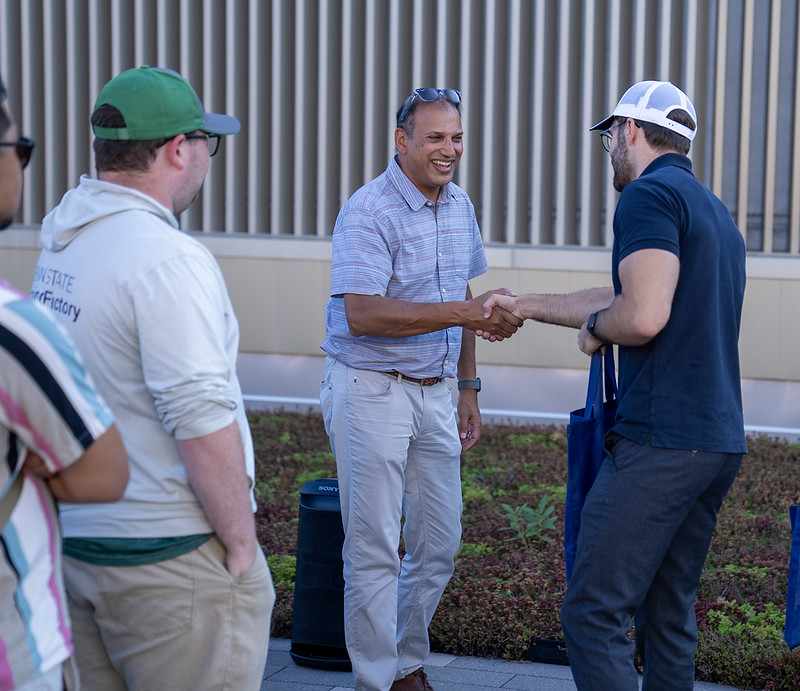 Two men smiling and shaking hands in an outdoor setting